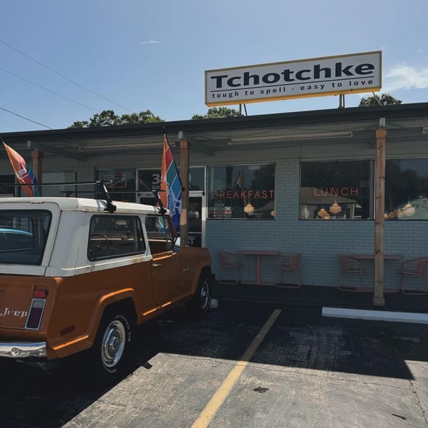 An orange and white Jeep parked in front of Tchotchke restaurant, with "Breakfast" and "Lunch" signs visible.