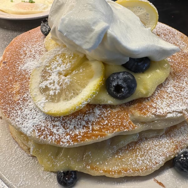 Stack of pancakes with lemon slices, blueberries, whipped cream, and powdered sugar.