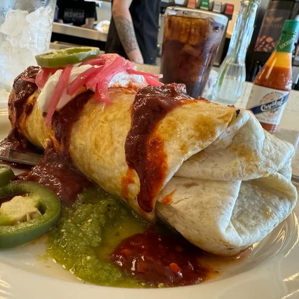 A large burrito covered in red sauce, sour cream, pickled onions, and a jalapeño slice.