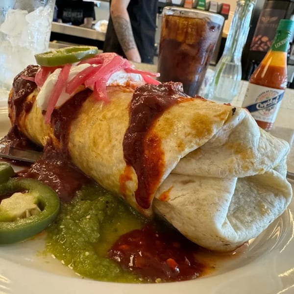 A large Tchotchke burrito covered in red sauce, sour cream, pickled onions, and jalapeños.
