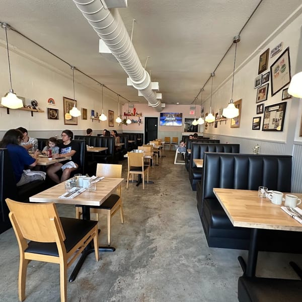 Interior of Tchotchke, an American restaurant, with black booths, wooden tables, and people dining.