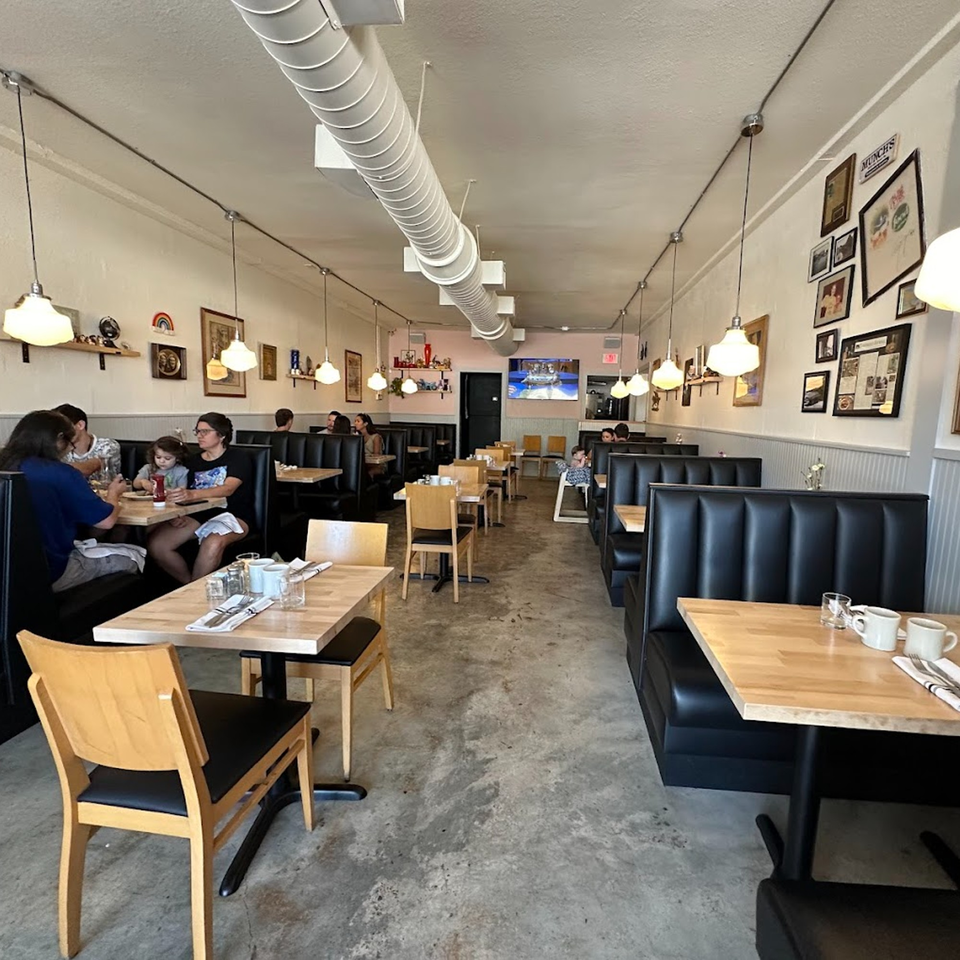 Interior of Tchotchke, an American restaurant, with black booths, wooden tables, and people dining.