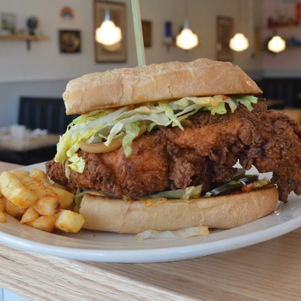 A large fried chicken sandwich with lettuce, onions, and pickles, served with golden fries.