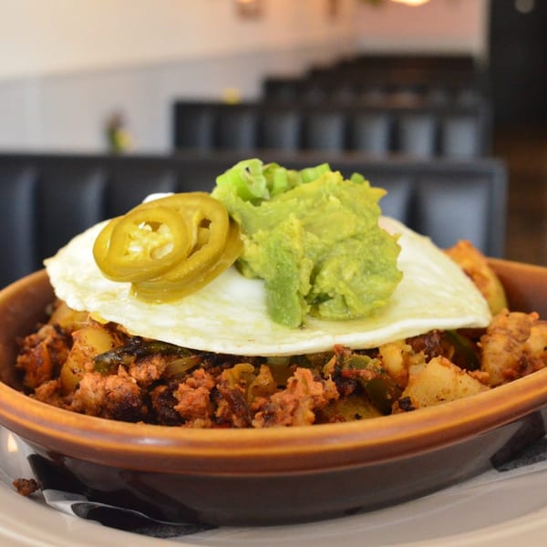 A close-up of a Tchotchke breakfast bowl with chorizo, potatoes, fried egg, jalapeños, and guacamole.
