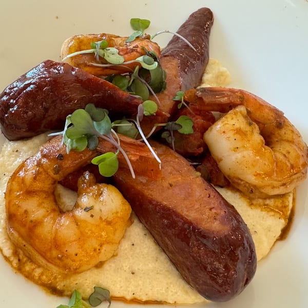 Shrimp and sausage with grits, garnished with microgreens, served on a white plate.