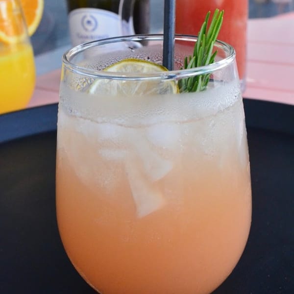 A refreshing Tchotchke cocktail with ice, lemon, and rosemary, on a dark tray.