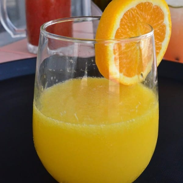 Close-up of a glass of orange juice garnished with an orange slice, with a red drink in the background.